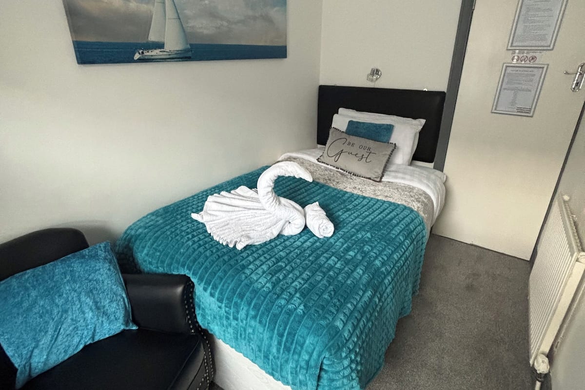 A hotel room with a bed, a chair, a painting, and a door with a sign.