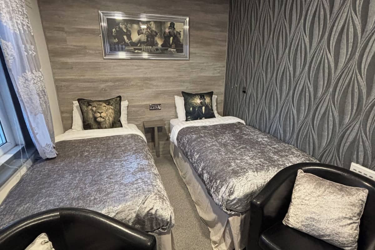 A hotel room with two beds, a sofa, a patterned wall, and a framed picture above the beds.
