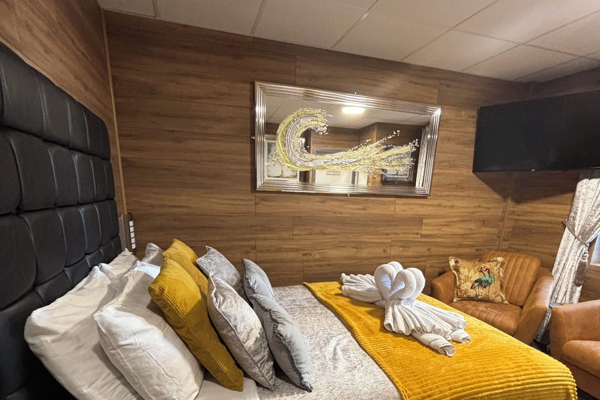 A bedroom with a bed, a wooden headboard, a mirror, a television, and a sofa.