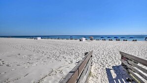 Una spiaggia con una passerella di legno, ombrelloni e lettini.