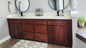 A bathroom with a wooden vanity, two round mirrors, a towel rack, and a soap dispenser. - Beautiful Modern Farmhouse
 (Keizer)