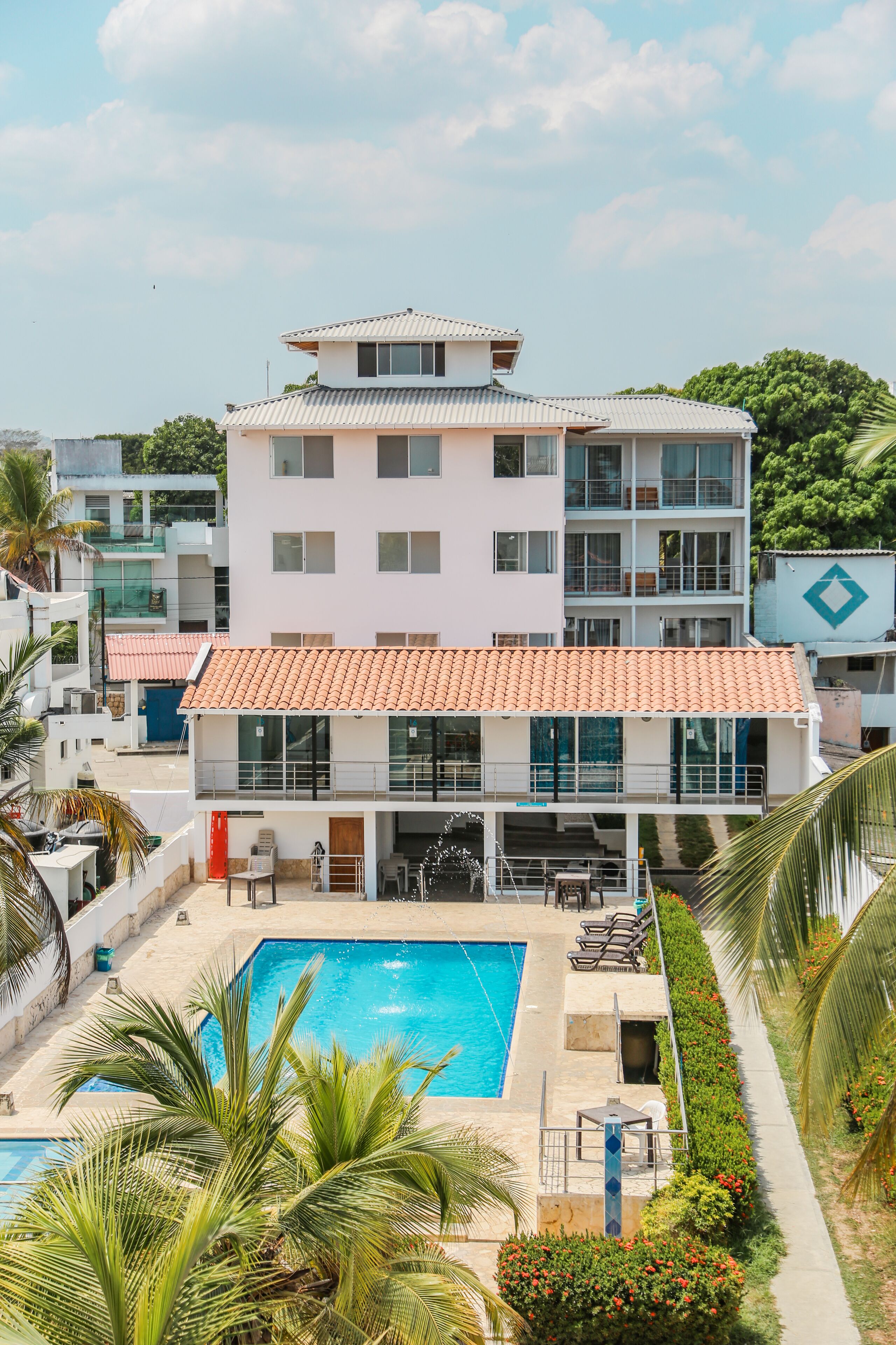 Un hotel moderno con piscina en la azotea, varios balcones y abundante vegetación.