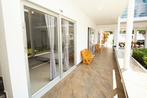 A corridor with sliding glass doors, wooden chairs, and a tiled floor. - Hotel Caribe Coveñas (Coveñas)
