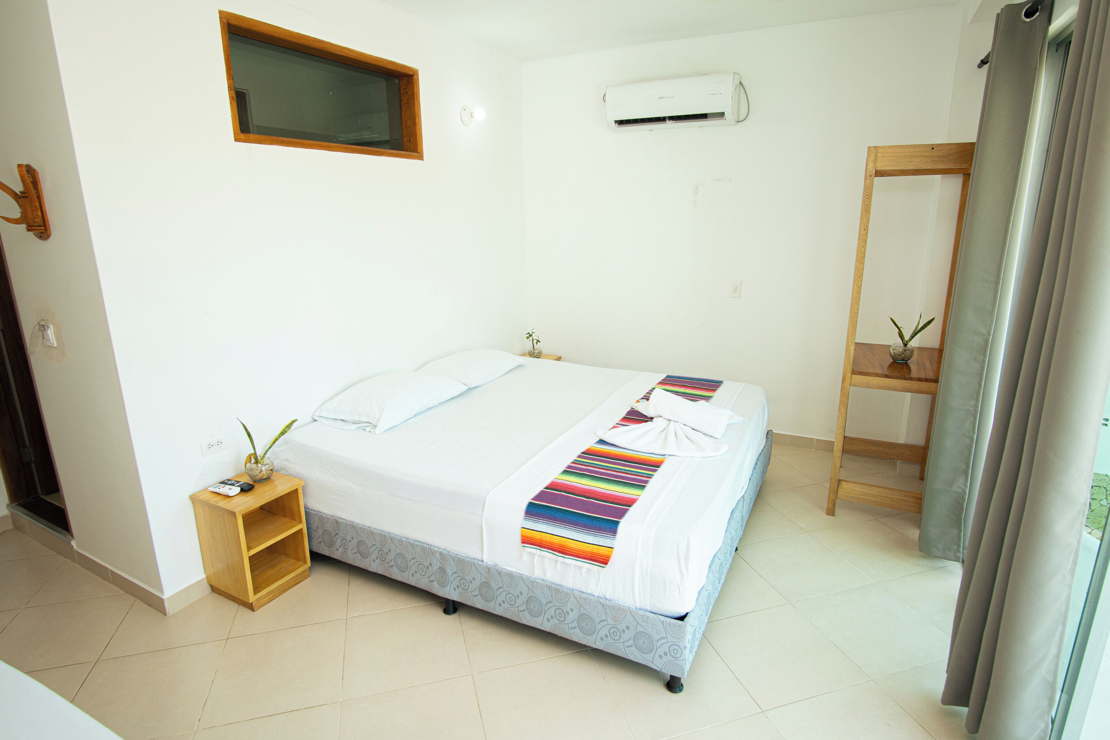 A bedroom with a bed, a nightstand, a window, an air conditioning unit, and a mirror.