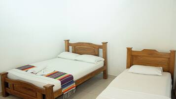 Una habitación con dos camas de madera, un ventilador de techo, un aire acondicionado y un televisor colgado en la pared.