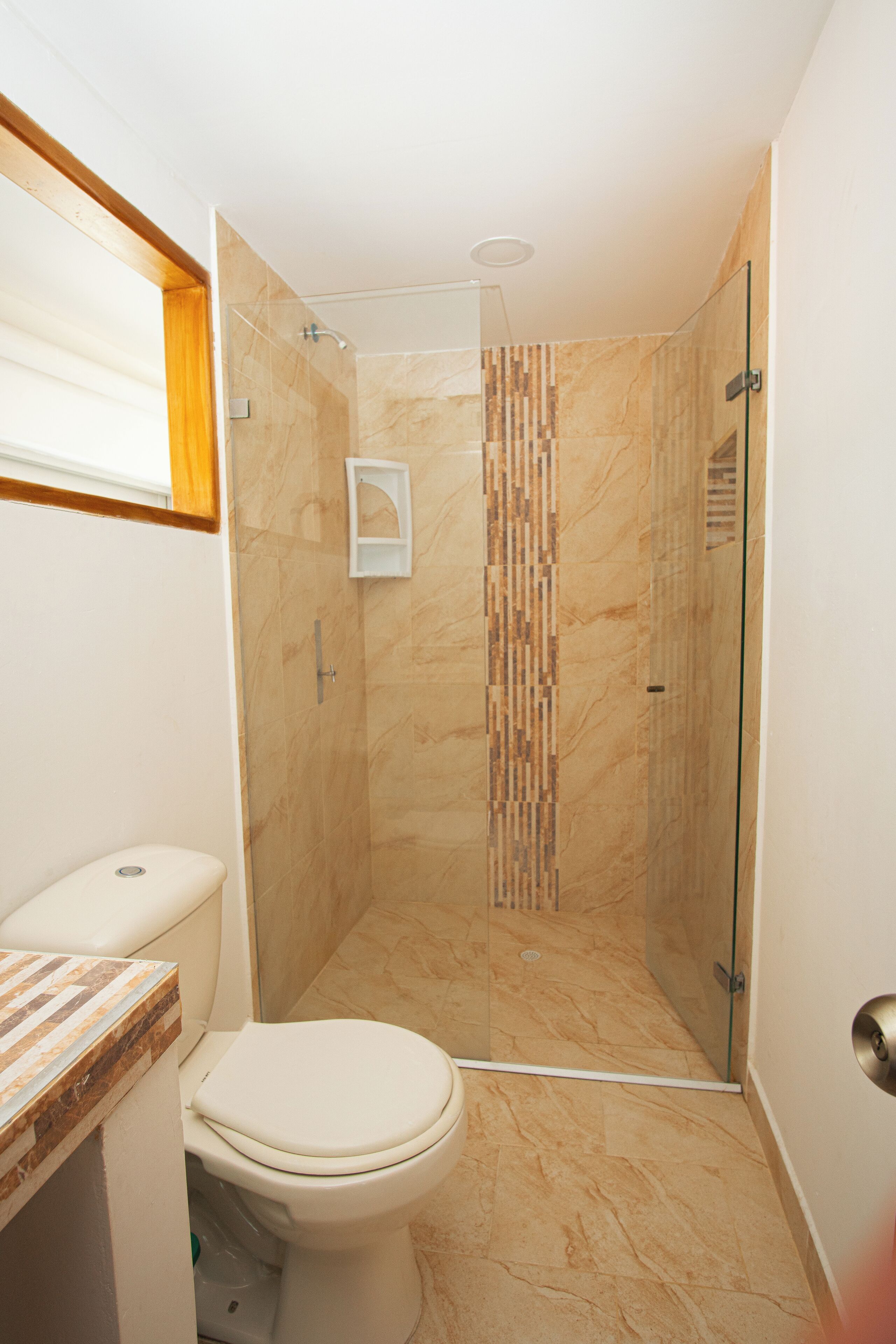 A bathroom with a toilet, a shower with a glass door, and a marble floor.
