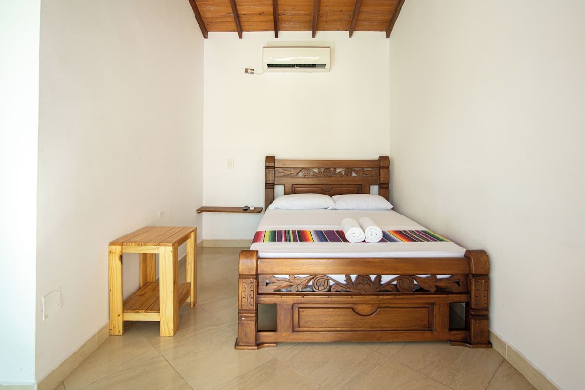 Un lit en bois avec une tête de lit, une petite table en bois et un ventilateur de plafond.