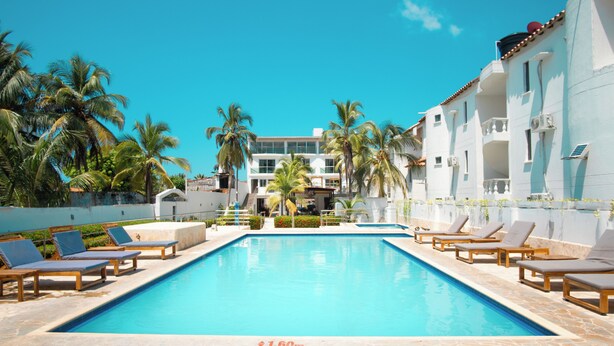 Una piscina con sillas de descanso, palmeras y un edificio con balcones.