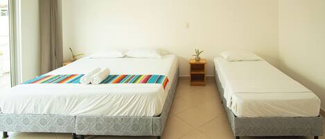 A hotel room with two single beds, a small bedside table with a plant, and a large window with curtains.