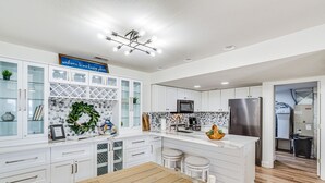 Una cocina moderna con armarios blancos, una mesa de comedor de madera y un refrigerador de acero inoxidable.