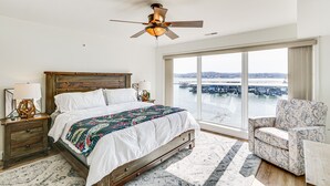 Un dormitorio con una cama grande, un ventilador de techo, vista a un puente y una silla junto a la ventana.