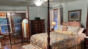 Una cama con dosel, un edredón floral, un aparador de madera y una mesita de noche.