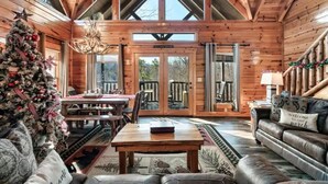 A cozy log cabin interior with a Christmas tree, wooden furniture, and a large window overlooking the outdoors. - 8 King Beds, 3 Levels, Hot tub, Pool table, Bar, Wood Soaker, Vaulted with VIEWS (Gatlinburg)
