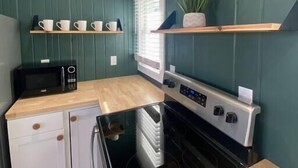 Een kleine keuken met een magnetron, oven en een houten aanrecht.