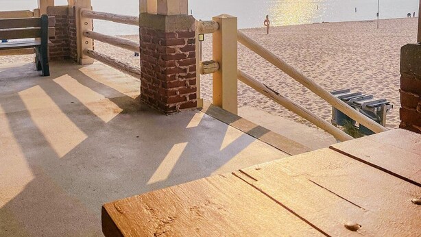 Een paviljoen aan het strand met een betonnen vloer, bakstenen pilaren en een houten bank.