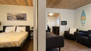 Een kamer met een houten plafond, een bed met een bedsprei met dessin, een bank en een muur met een surfboard decoratie.