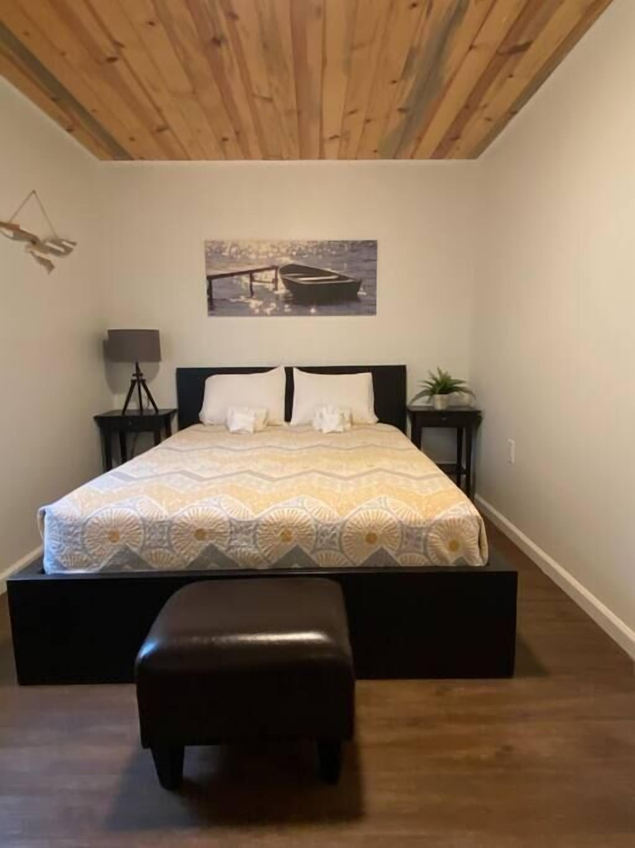 Um quarto com uma cama, um banquinho, um abajur e um quadro na parede.