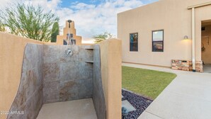 Un espace de douche extérieur moderne, agrémenté d’un mur en pierre et offrant une vue dégagée sur un bâtiment doté d’un toit plat et d’une petite pelouse.