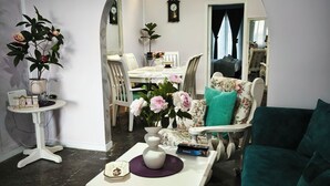 A living room with a white sofa, a coffee table with a vase and a book, a dining area with a white table and chairs, and a mirror on the wall. - Ένα ευχάριστο χώρο άνετο και εξυπηρέτηκο έχει όλες της άνεσης...μέσα στην πόλη.. (Kastelli)