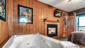 A wooden-paneled room with a large bathtub, a fireplace, and framed pictures on the walls. - King Bed, Pool Table, Hot tub, Vinyl Record Player, Covered Back Porch w VIEWS!! (Sevierville)