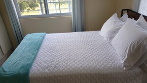 Una cama con un colchón blanco acolchado y una manta color turquesa.