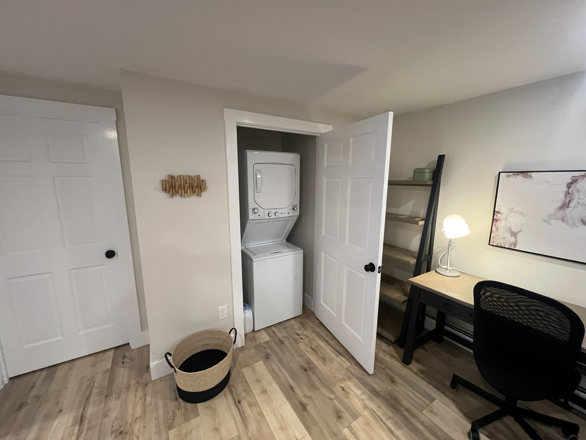 A room with a washing machine, a desk with a chair, and a basket on the floor.