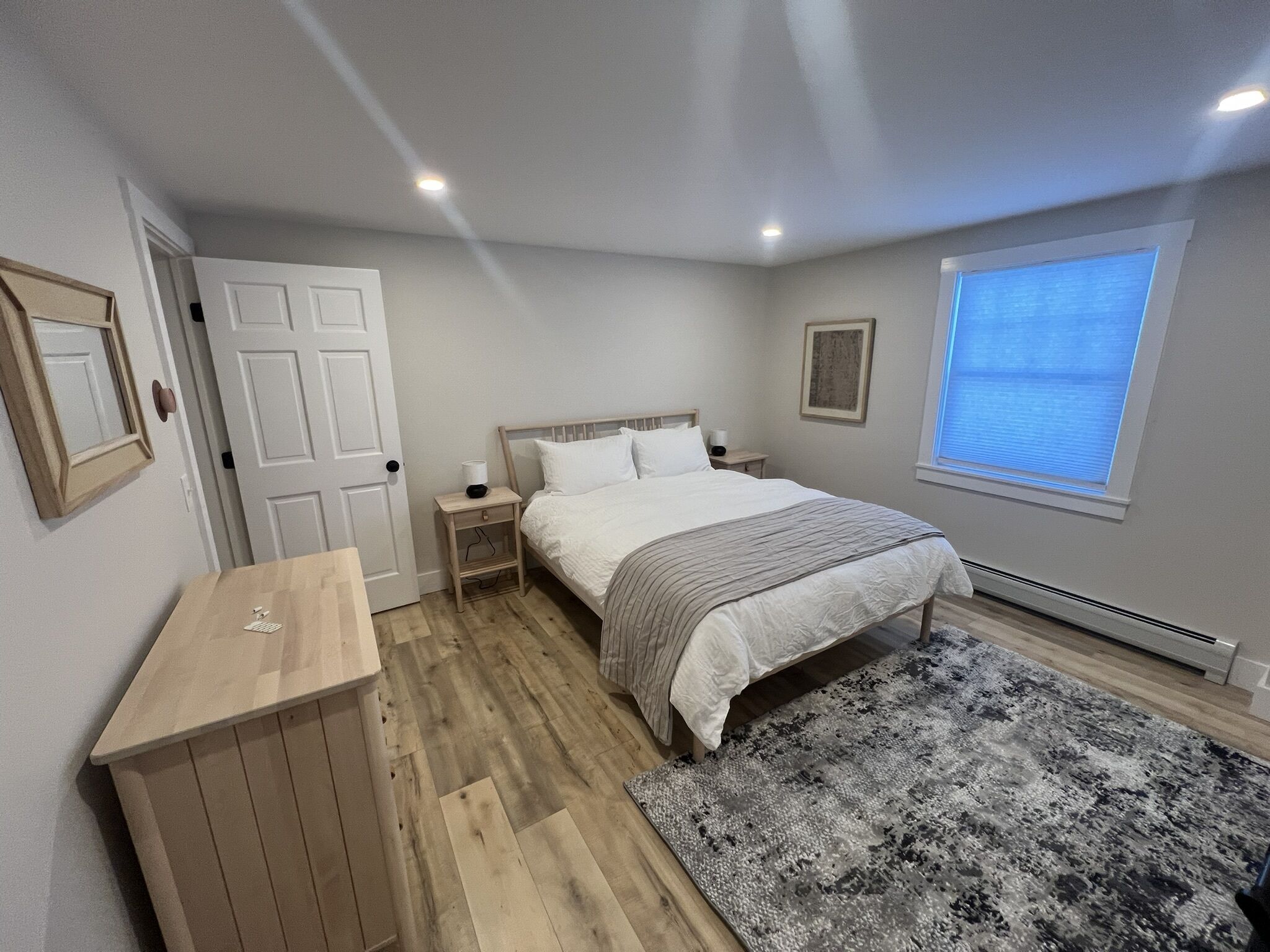 A bedroom with a bed, bedside tables, a desk, a window with blinds, and a radiator.