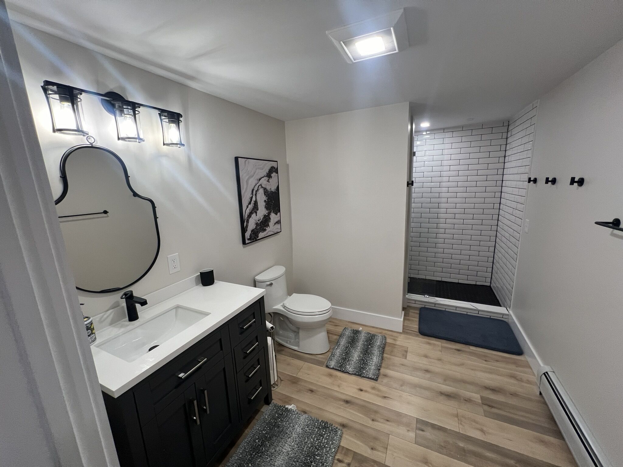 Een moderne badkamer met een witte wastafel, zwarte kastjes, een wit toilet en een douche met een muur van witte bakstenen.