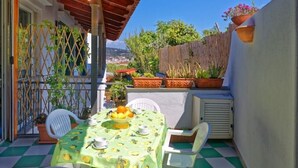 A patio with a table set for two, surrounded by potted plants and a view of the city. - La Bella Forianella. Alloro (Forio)