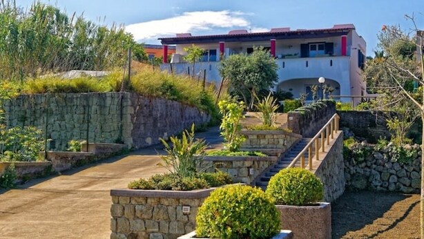 A modern building with a stone retaining wall, a paved driveway, and a staircase leading to a balcony. - La Bella Forianella. Alloro (Forio)