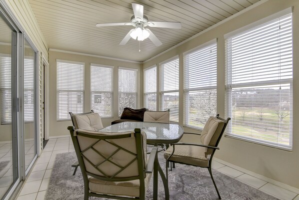A sunroom with a glass door, a ceiling fan, a dining table with chairs, and large windows with blinds.