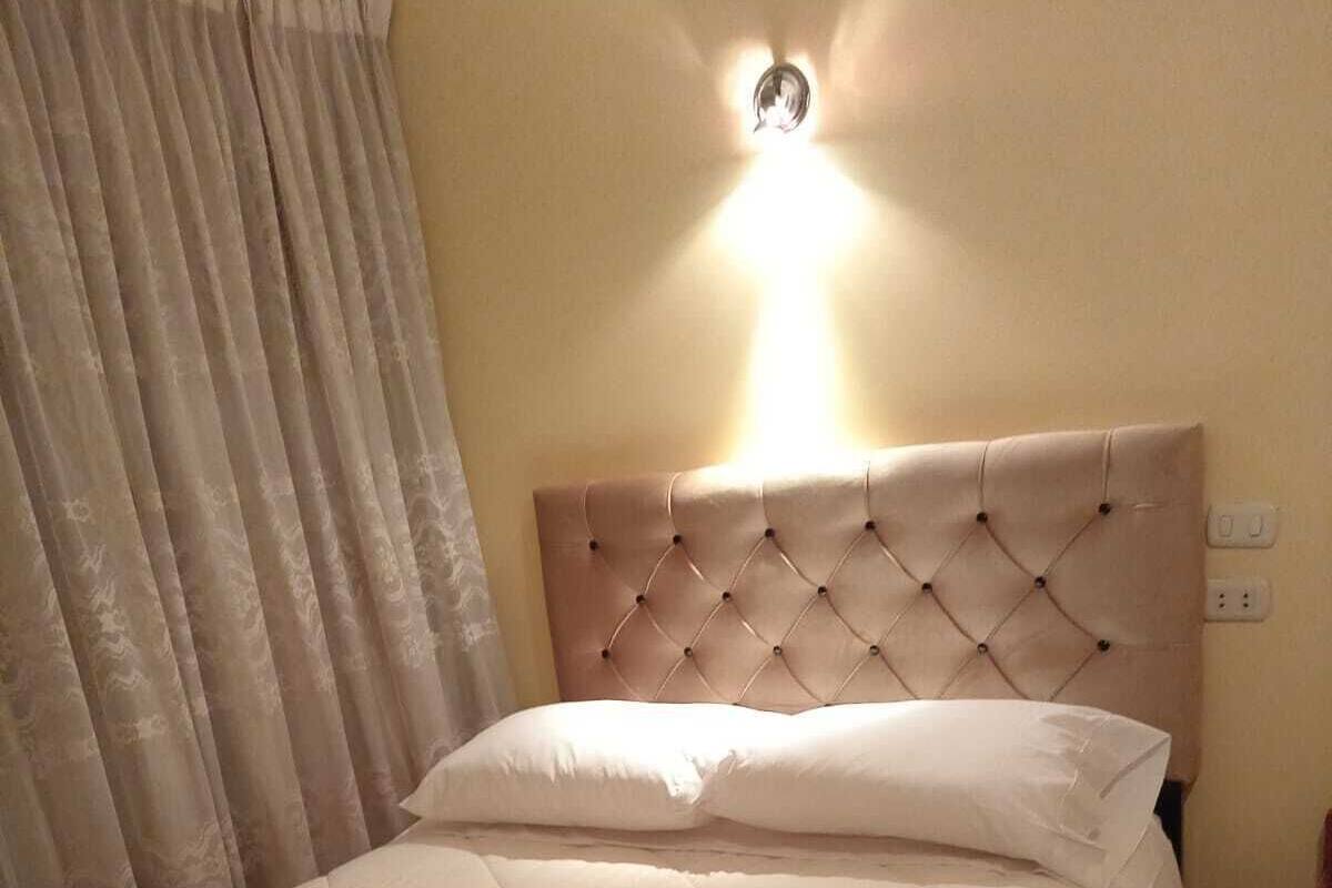 A hotel room with a bed, a wall-mounted light, and a patterned floor.