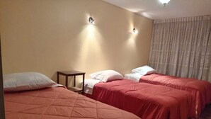 Habitación de hotel con dos camas, cada una con cubrecama rojo y almohadas blancas. Hay dos lámparas fijadas a la pared y una mesita de noche de madera.