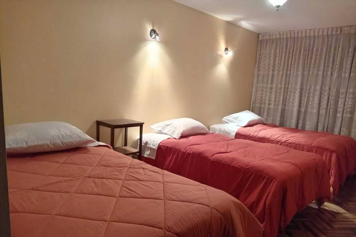 A hotel room with two beds, each with a red bedspread and white pillows. There are two wall-mounted light fixtures and a small wooden nightstand.