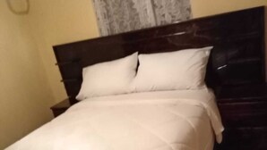 Una cama bien tendida con edredón y almohadas blancos, cabecera de madera y suelo estampado.