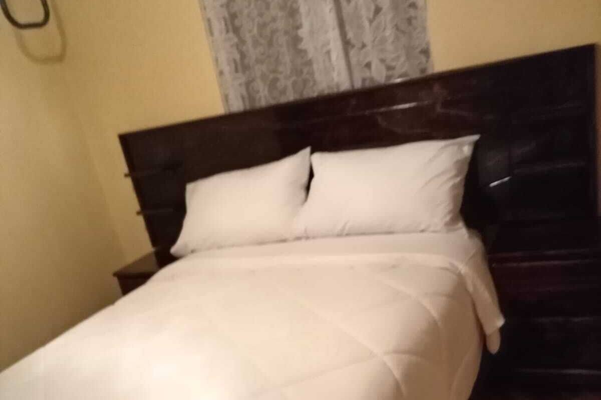 A neatly made bed with a white duvet and pillows, a wooden headboard, and a patterned floor.