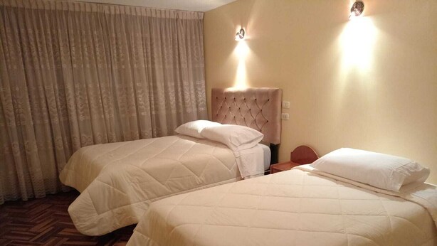 Habitación de hotel con dos camas, piso de madera en espiga y un gran ventanal con cortinas.