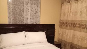 Una cama con un edredón blanco acolchado, un cabecero de madera oscura y una mesita de noche con una lámpara.
