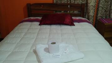A neatly made bed with a white duvet, a red pillow, and a rolled-up towel.