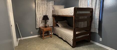 Une chambre avec un lit superposé, un ventilateur de plafond, une petite table de chevet en bois et une lampe.