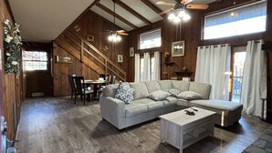 A spacious living area with a wooden floor, a grey sofa set, a coffee table, and a ceiling fan.