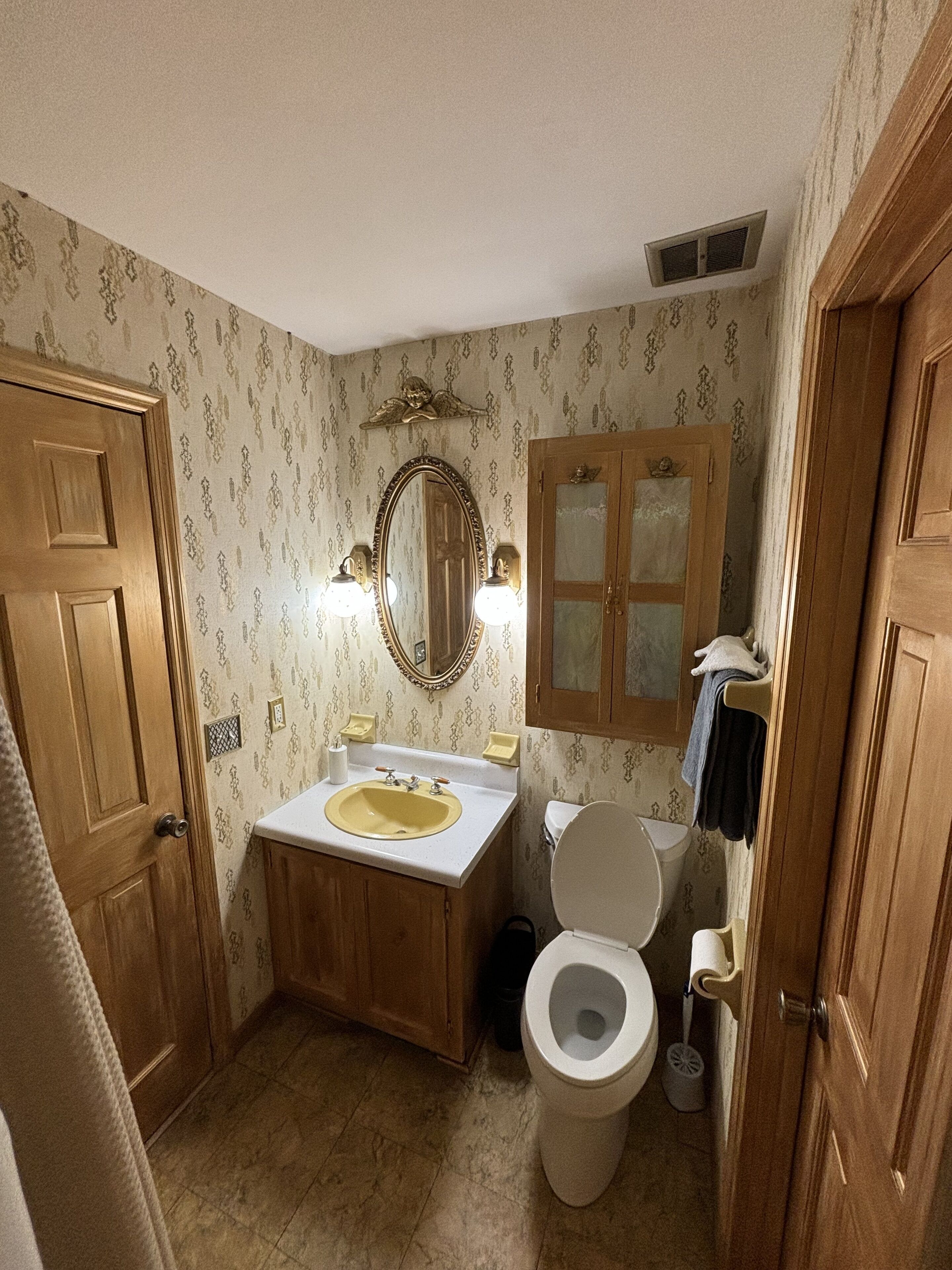 A bathroom with a wooden vanity, a sink, a toilet, and a mirror with lights.