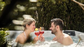 Een stel in een jacuzzi, met een glas rode drank, omringd door groen.
