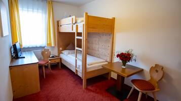 Ein Zimmer mit Etagenbett, Schreibtisch mit Laptop, Stuhl, kleinem Tisch mit Blumenvase und einem Fenster mit Vorhängen.
