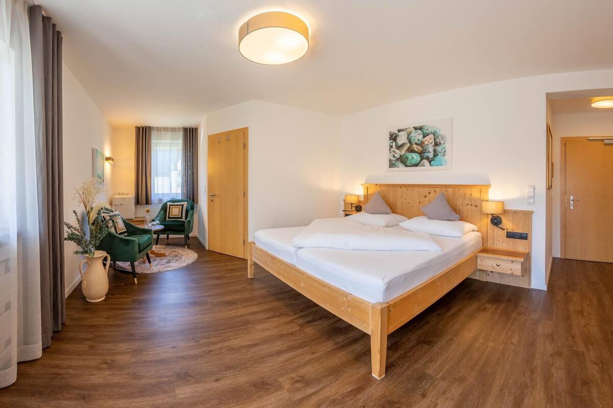 Une chambre à coucher avec un lit en bois, un bureau et une chaise. Il y a une porte et une fenêtre avec des rideaux.