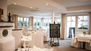 Een restaurant met meerdere tafels voor diners, een krijtbordmenu en grote ramen voor natuurlijk licht.