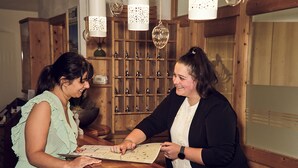 Twee personen bij een houten receptiebalie, met een prikbord en decoratieve objecten.
