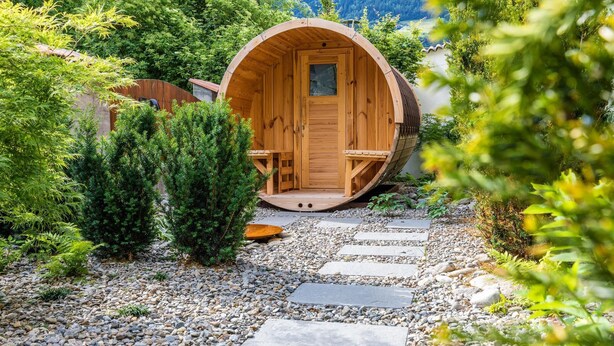Een houten hutje met een ronde ingang, omringd door een tuin met een grindpad ernaartoe.