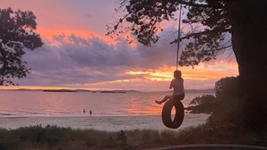 Iemand zwaait op een autobandschommel met uitzicht op een strand bij zonsondergang.