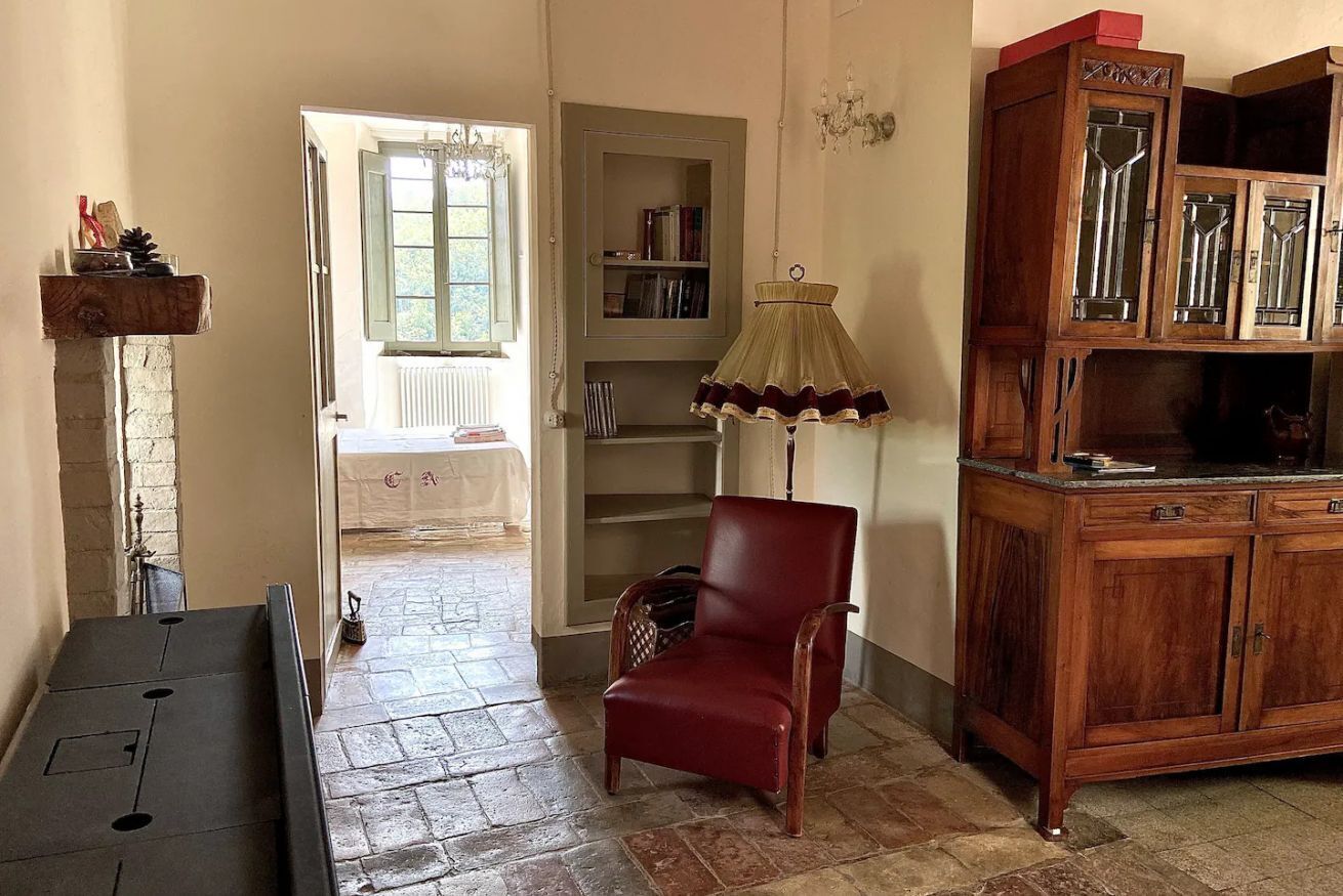 Een kamer met een open haard, een rode fauteuil, een houten kast en een boekenkast.